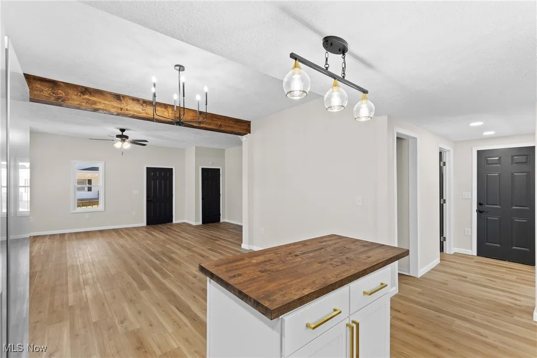 Kitchen featuring wood counters, white cabinets, beam ceiling, hanging light fixtures, and open floor plan