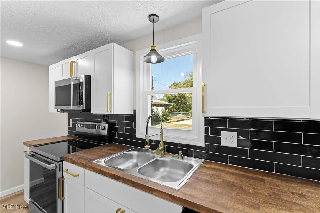 Kitchen with stainless steel appliances, tasteful backsplash, white cabinetry, butcher block countertops, and a textured ceiling