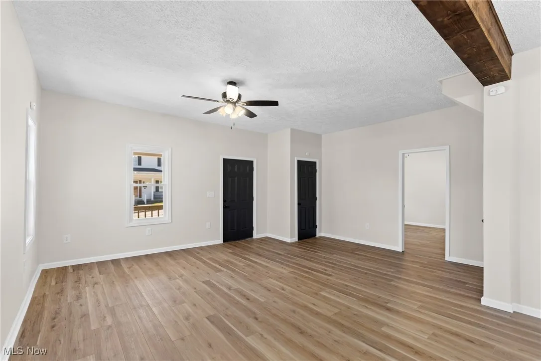 Unfurnished bedroom featuring a textured ceiling, light wood-type flooring, a ceiling fan, and beamed ceiling