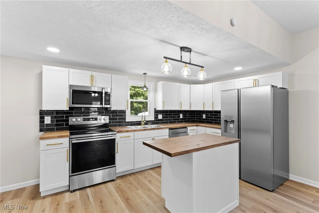 Kitchen featuring a kitchen island, white cabinets, appliances with stainless steel finishes, decorative backsplash, and a textured ceiling