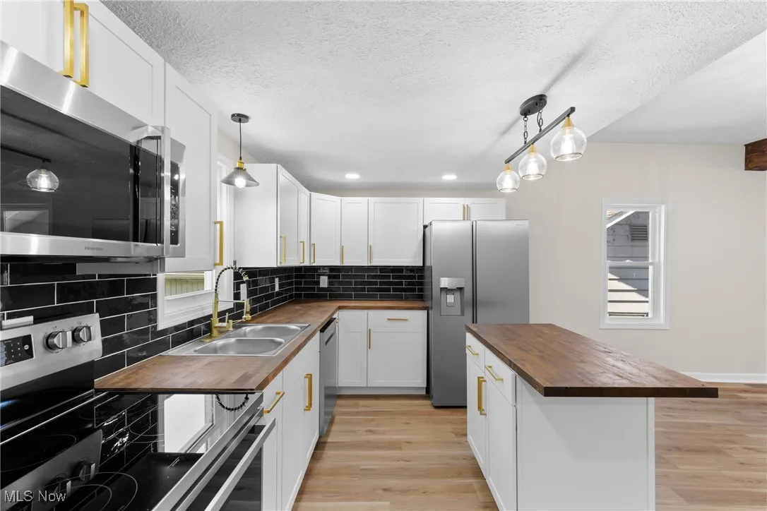 Kitchen with appliances with stainless steel finishes, butcher block countertops, decorative backsplash, white cabinets, and healthy amount of natural light