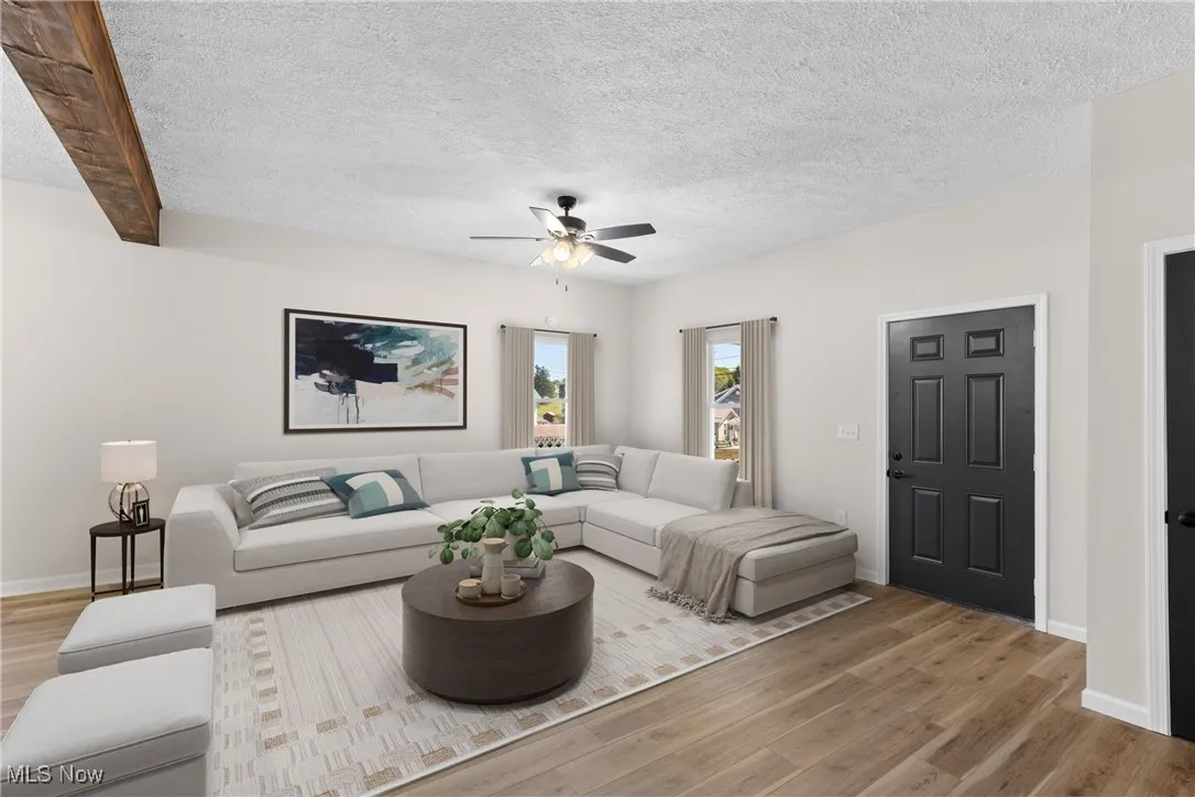 Living room with a textured ceiling, light wood-style floors, and a ceiling fan
