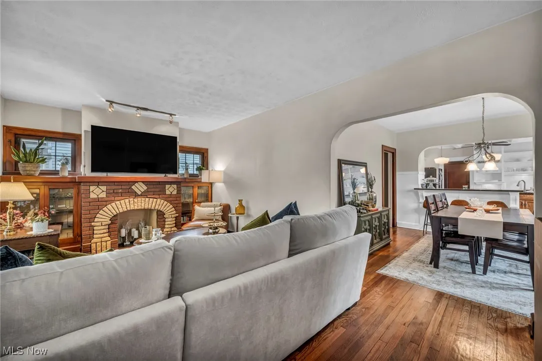 Living area featuring wood-type flooring, a chandelier, arched walkways, a brick fireplace, and track lighting