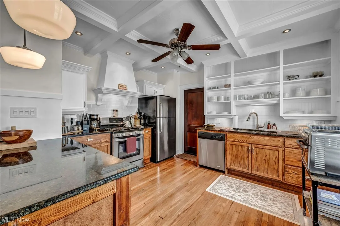Kitchen with open shelves, decorative backsplash, dark stone countertops, stainless steel appliances, and beamed ceiling