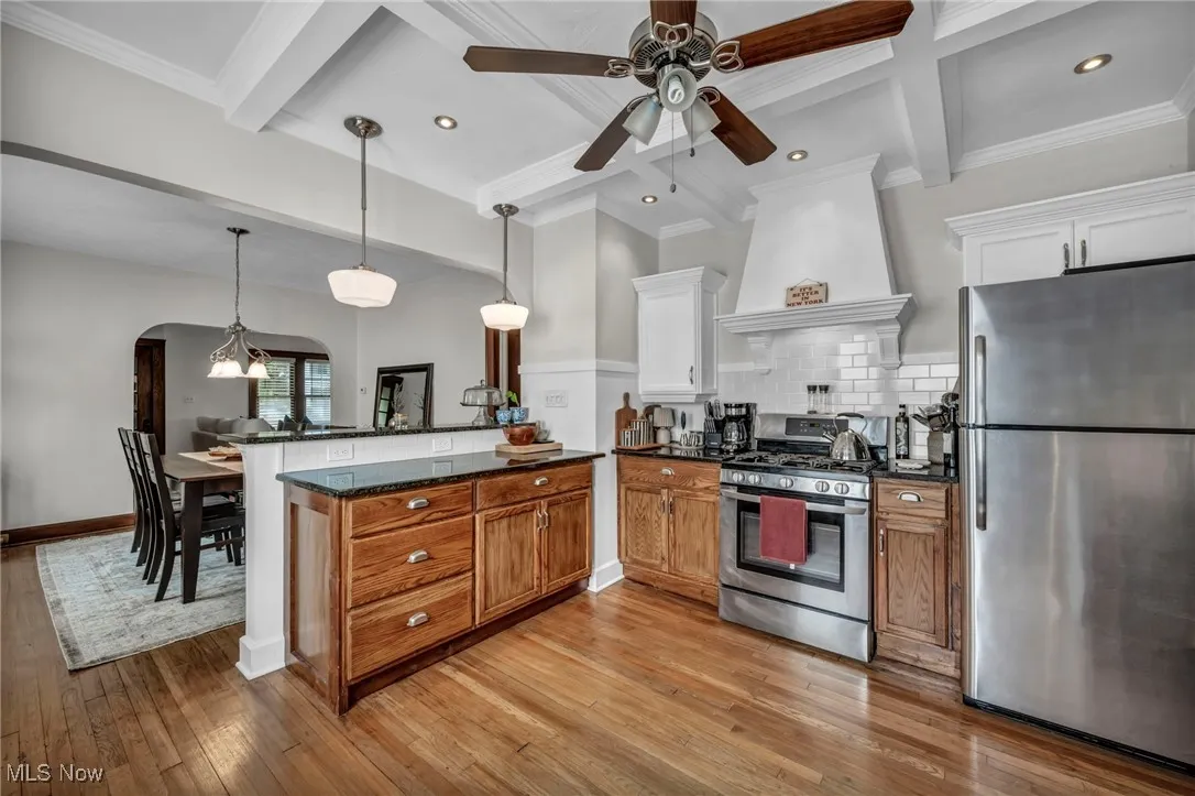 Kitchen with beam ceiling, stainless steel appliances, a peninsula, pendant lighting, and dark stone counters