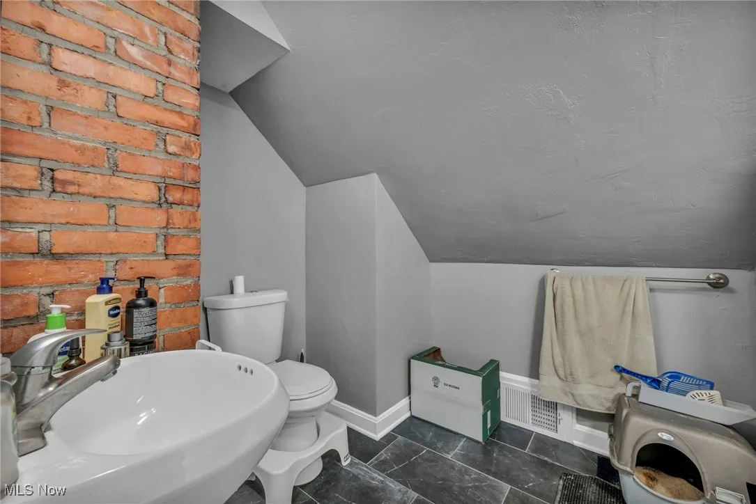 Half bathroom with lofted ceiling and brick wall