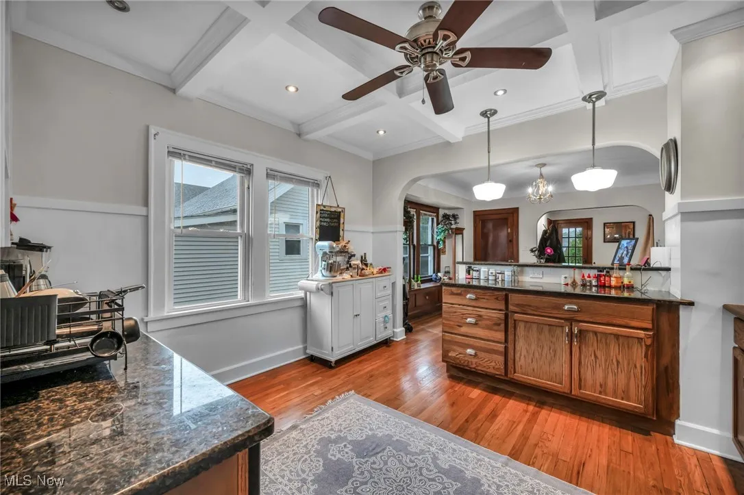 Kitchen with dark stone counters, brown cabinets, light wood-style flooring, coffered ceiling, and beam ceiling