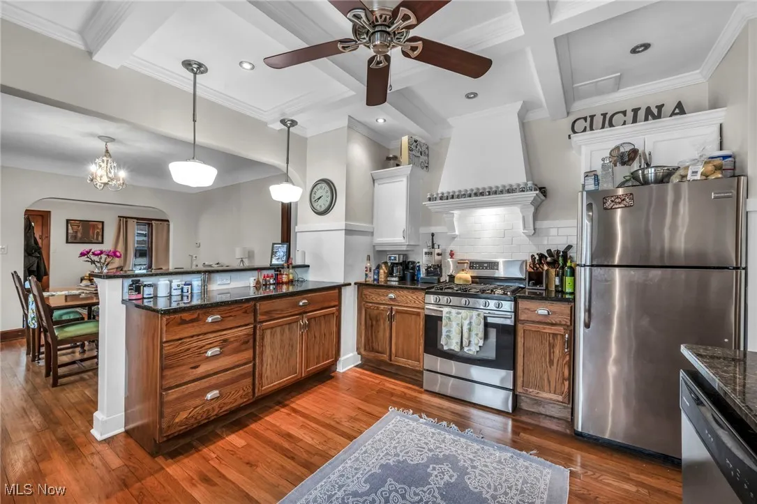 Kitchen with tasteful backsplash, appliances with stainless steel finishes, beamed ceiling, coffered ceiling, and a peninsula