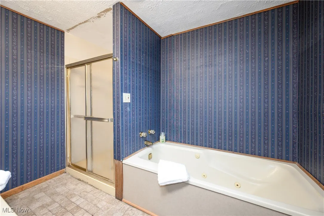 Full Primary bath with a textured ceiling, wallpapered walls, a tub with jets, and a shower stall
