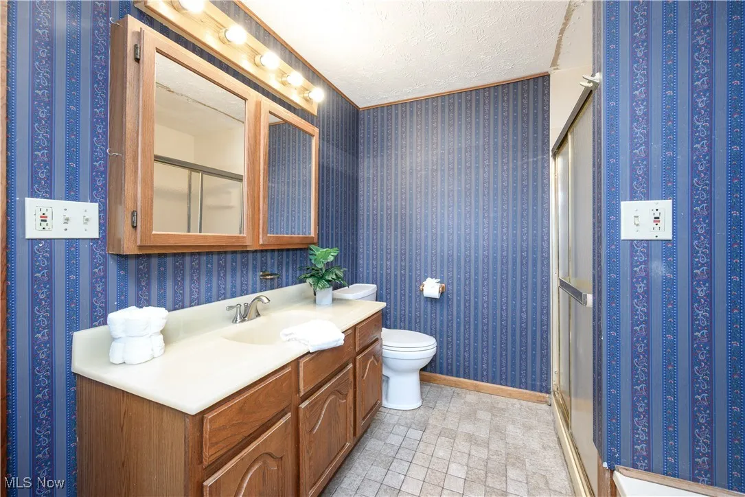 Full bath featuring a shower stall, vanity, a textured ceiling, and wallpapered walls