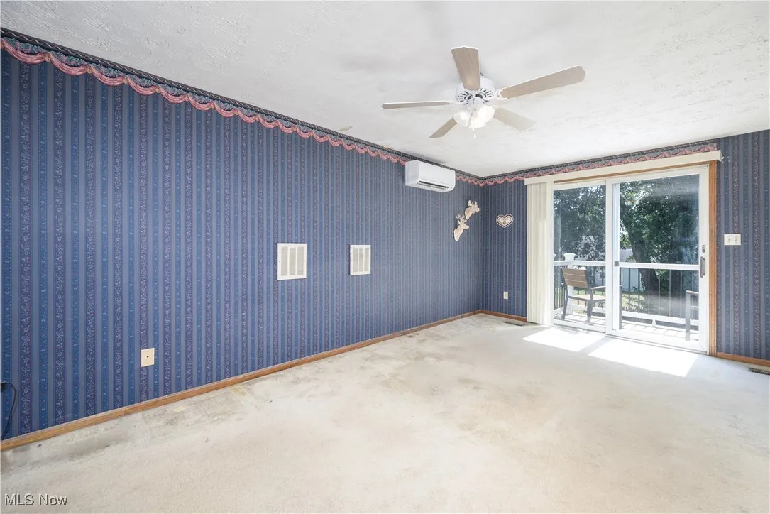 Carpeted primary bedroom featuring wallpapered walls, a textured ceiling, and a ceiling fan and mini split AC unit
