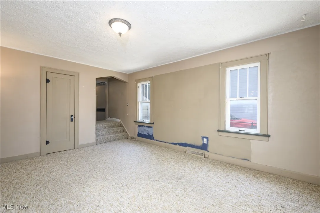 Living room with a textured ceiling, carpet floors, closet and stairway