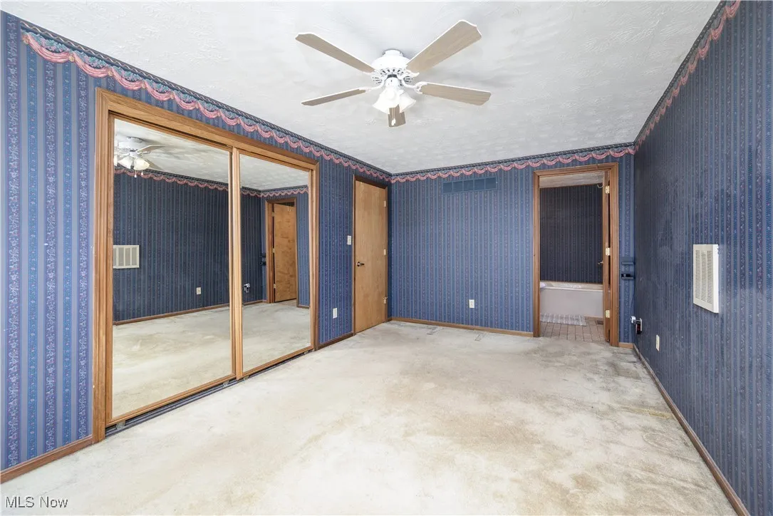 Carpeted Primary bedroom featuring wallpapered walls, a textured ceiling, and ceiling fan