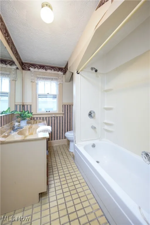 Second floor bathroom featuring wallpapered walls,  shower combination, a textured ceiling, double vanity