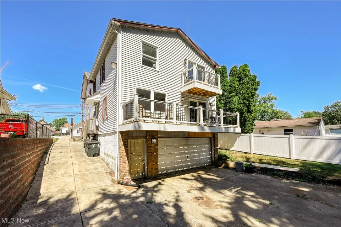 Back of property with an attached garage, a balcony, concrete driveway, and brick siding