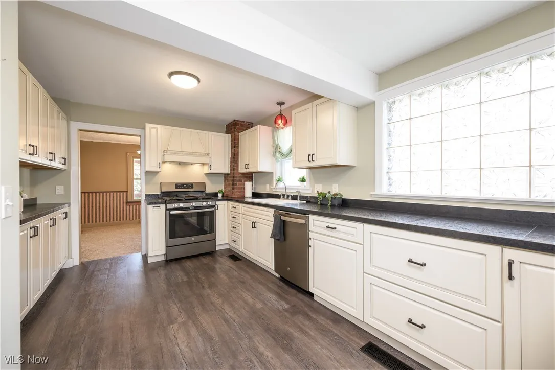 Kitchen featuring dark countertops, stainless steel appliances, custom range hood and waterproof luxury vinyl floor