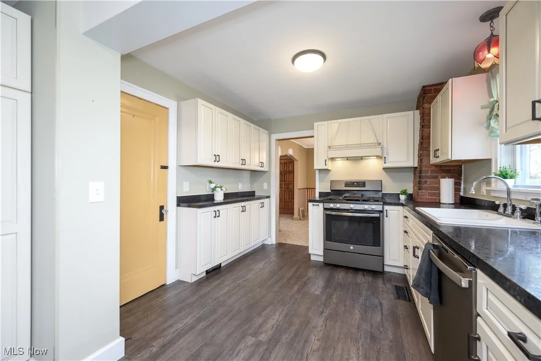 Kitchen with stainless steel appliances, dark wood finished floors, custom range hood, and white cabinetry