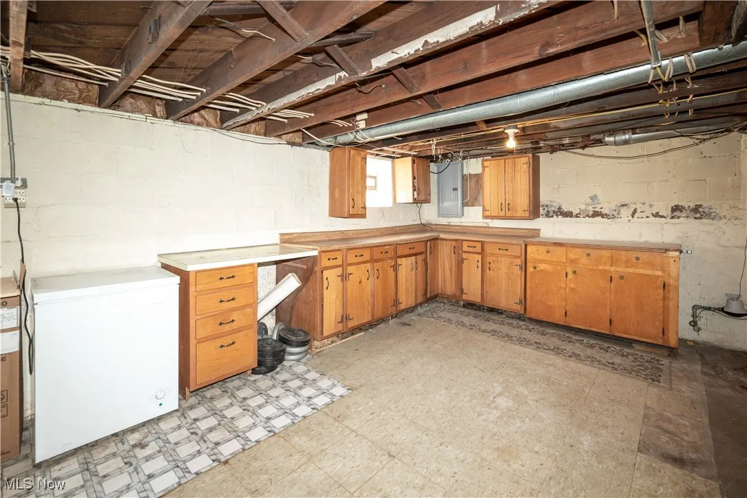 Basement featuring light flooring, light countertops, electric panel, and brown cabinets