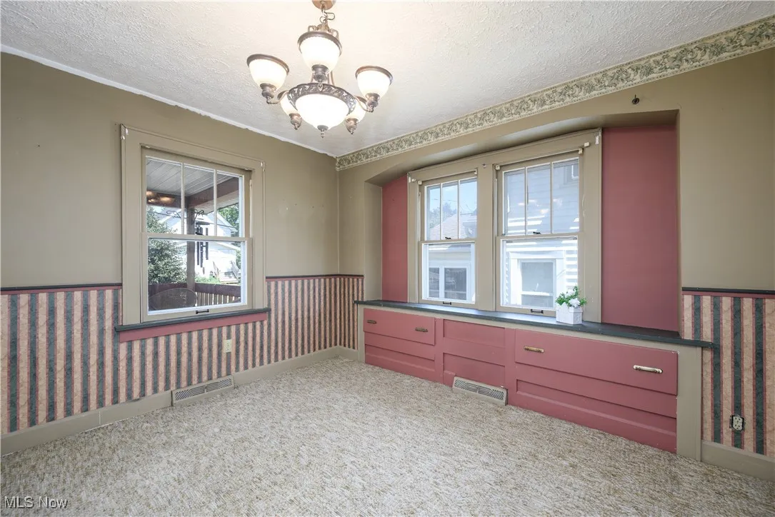 Dining room featuring a textured ceiling, carpet flooring, a chandelier, built in drawers and window seat