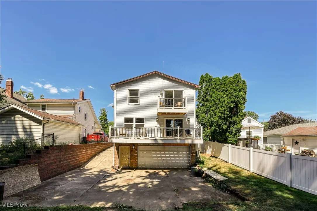 Back of house featuring a fenced backyard, a balcony, and an attached garage