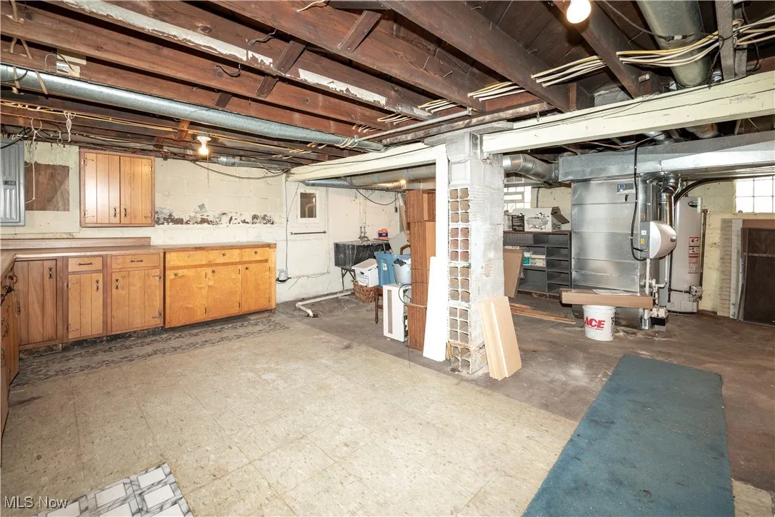 Unfinished below grade area featuring light flooring, water heater, furnace and electric panel