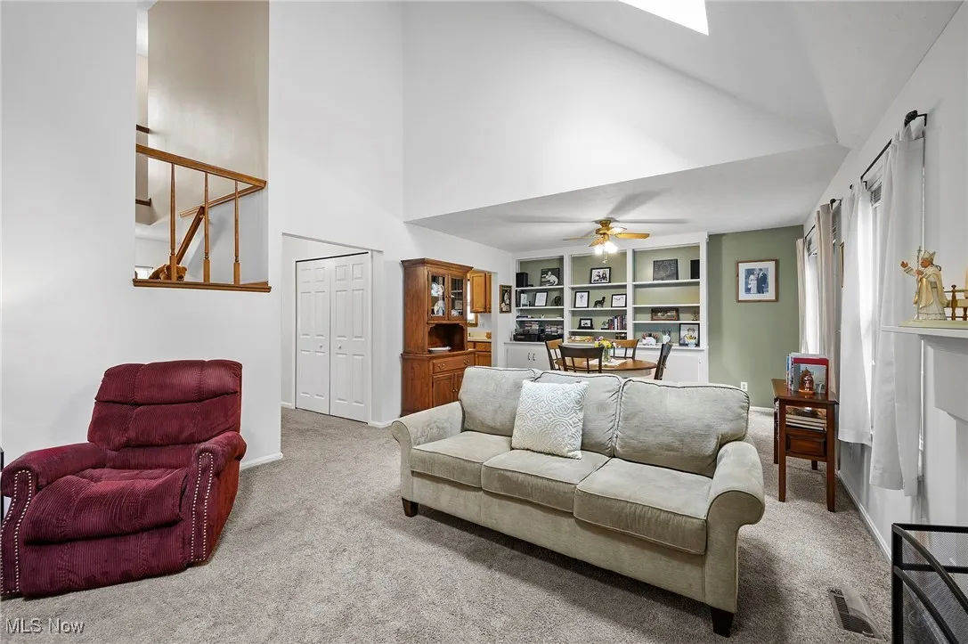 Living area featuring high vaulted ceiling, carpet flooring, ceiling fan, stairway, and a skylight