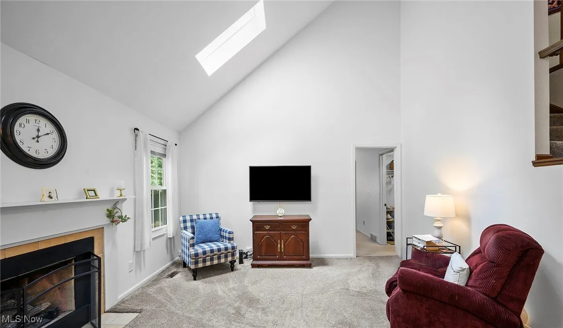 Living room featuring carpet floors, high vaulted ceiling, a fireplace, and a skylight