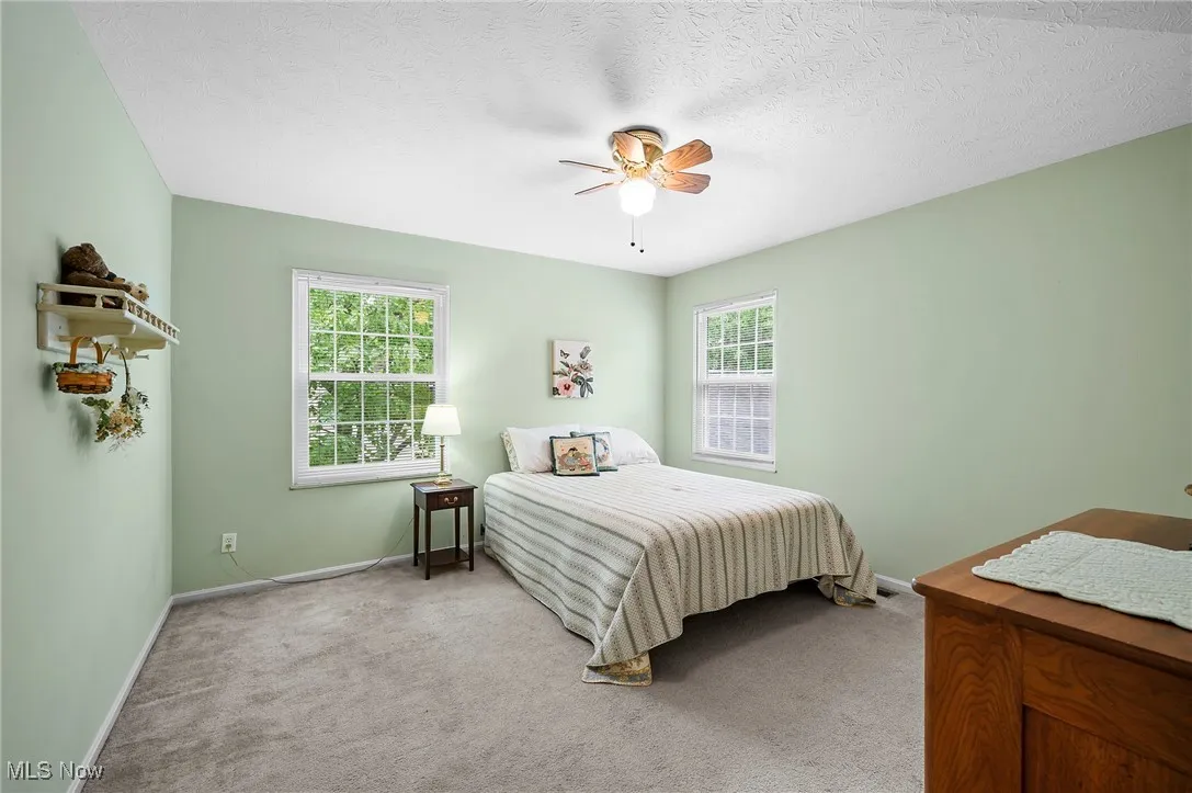 Carpeted bedroom featuring multiple windows, ceiling fan, and a textured ceiling