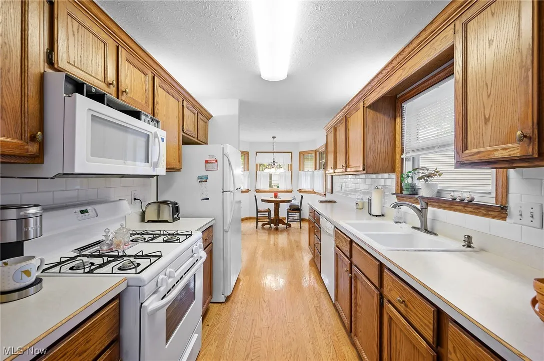 Kitchen featuring white appliances, brown cabinetry, light countertops, backsplash, and a textured ceiling