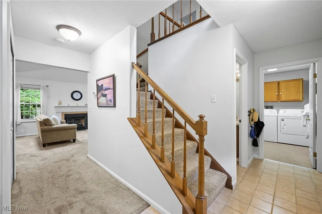 Stairs featuring carpet floors, separate washer and dryer, a glass covered fireplace, a textured ceiling, and tile patterned floors