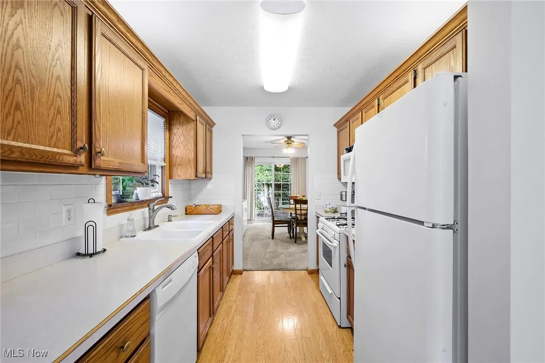 Kitchen with white appliances, light countertops, brown cabinetry, ceiling fan, and a textured ceiling