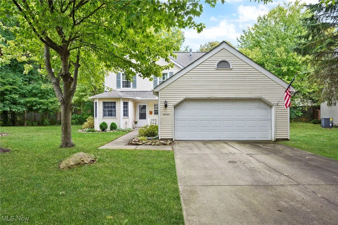 Traditional home with a front lawn, an attached garage, concrete driveway, and a shingled roof