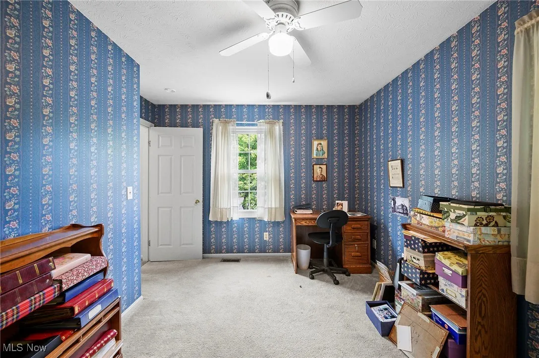 Carpeted office with wallpapered walls, a textured ceiling, and ceiling fan
