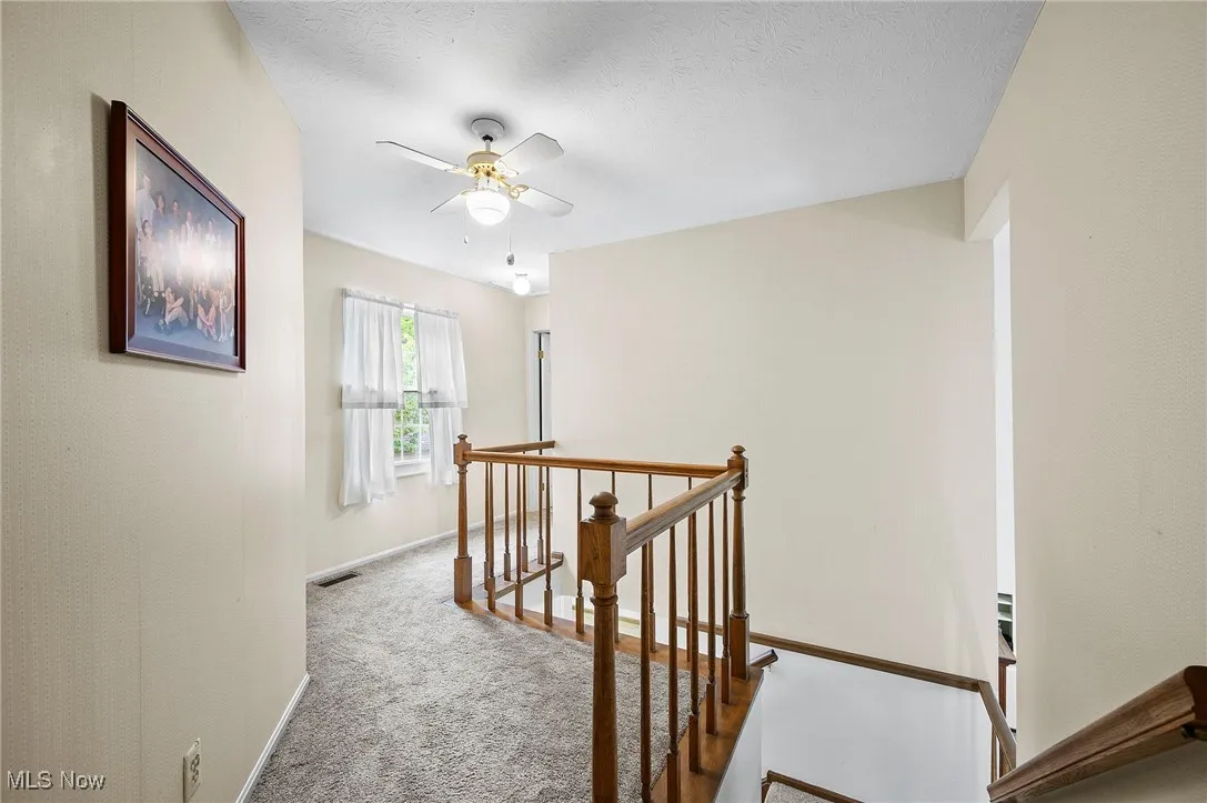 Hall featuring an upstairs landing, carpet flooring, and a textured ceiling