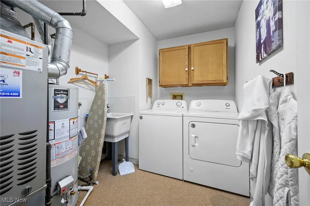 Laundry area featuring heating unit, cabinet space, water heater, and washer and dryer
