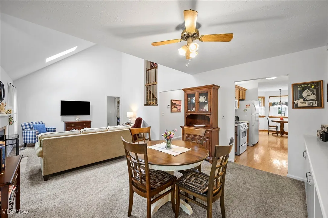 Dining room with lofted ceiling, light colored carpet, ceiling fan, and a skylight