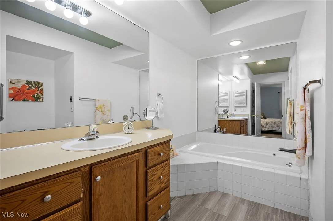 Full bath with ensuite bathroom, vanity, a garden tub, and light wood-style floors