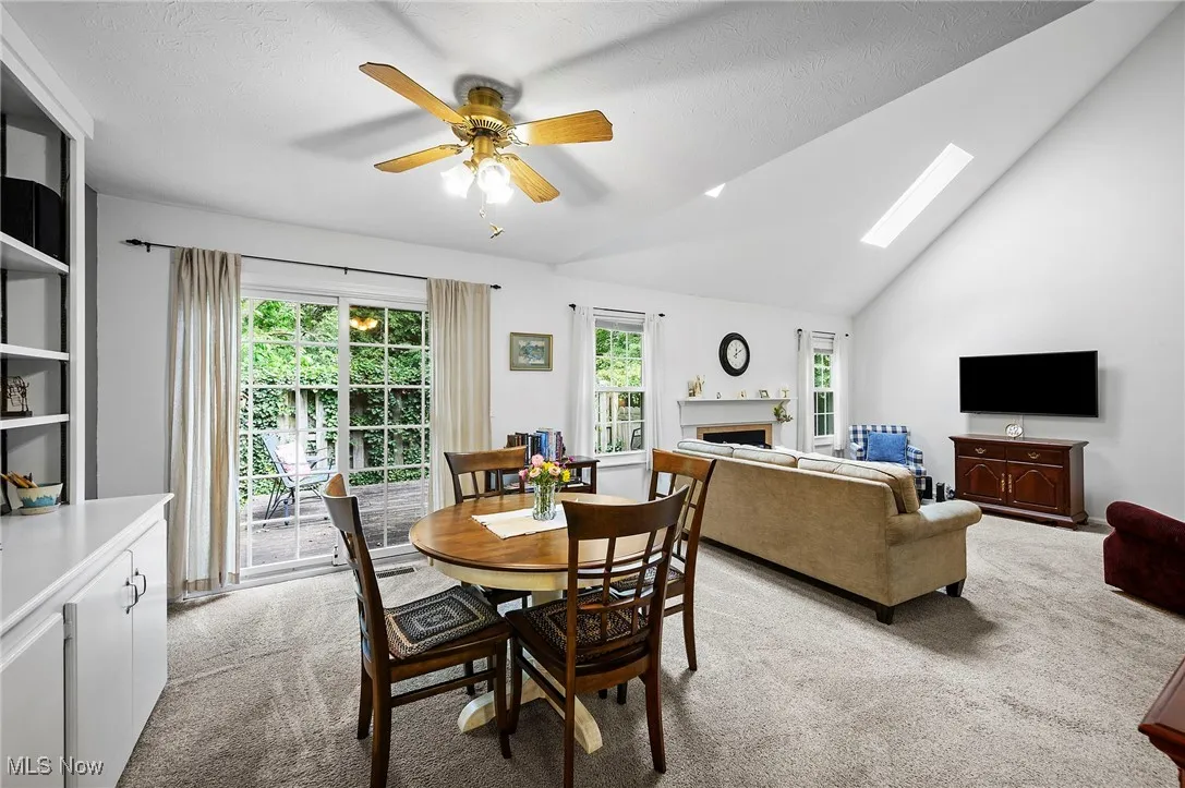 Dining space featuring light carpet, a fireplace, ceiling fan, high vaulted ceiling, and a skylight