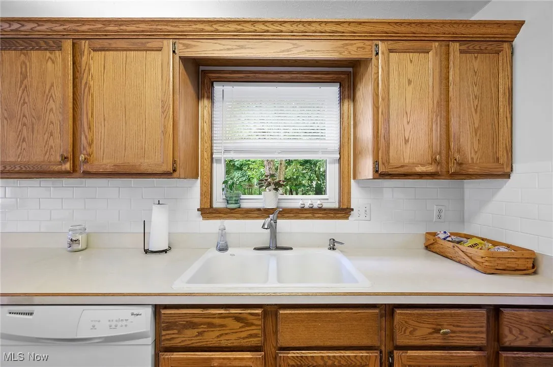 Kitchen featuring light countertops, dishwasher, backsplash, and brown cabinets