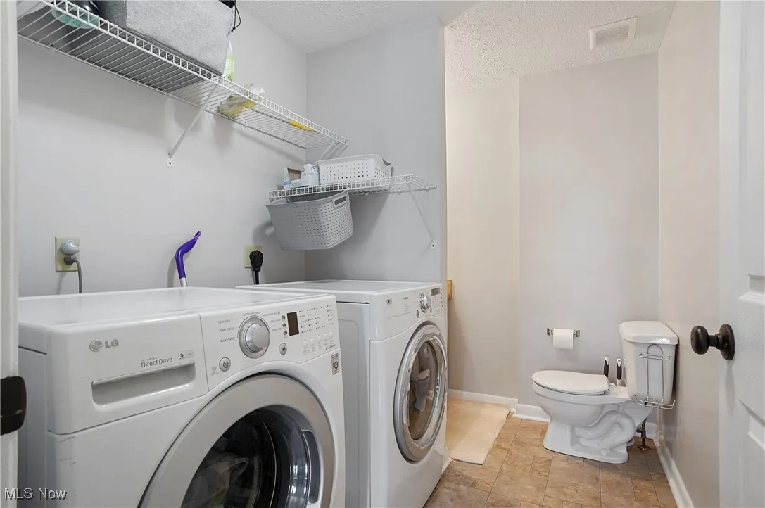 Laundry room with a textured ceiling, washing machine and dryer, and light tile patterned floors