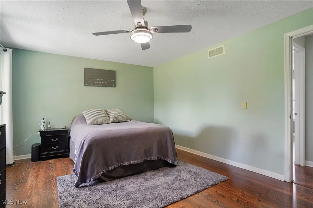 Bedroom with a textured ceiling, dark wood finished floors, and ceiling fan