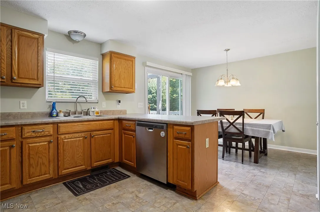 Kitchen with a peninsula, brown cabinets, stainless steel dishwasher, a chandelier, and a textured ceiling