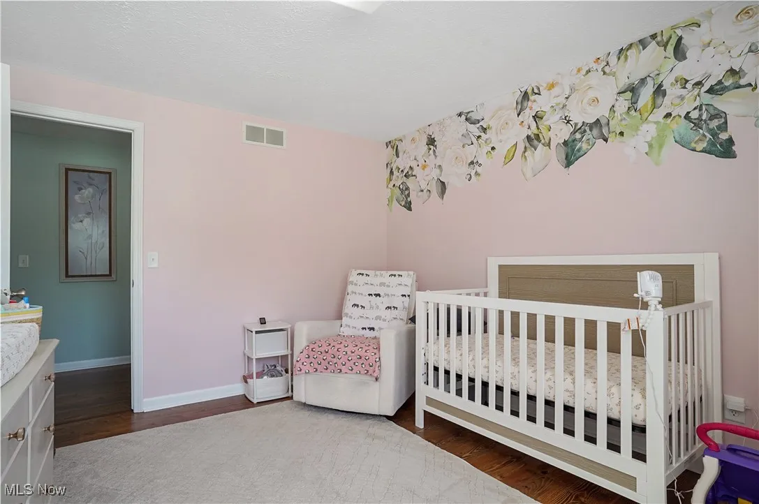 Bedroom with dark wood-style floors, a nursery area, and a textured ceiling