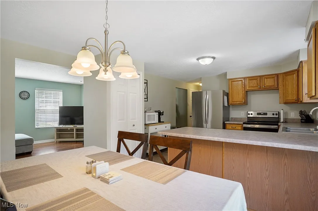 Kitchen featuring light countertops, a peninsula, appliances with stainless steel finishes, decorative light fixtures, and a chandelier