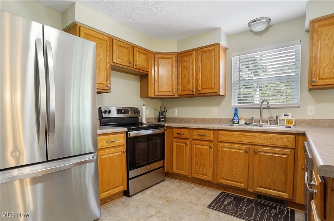 Kitchen with appliances with stainless steel finishes, brown cabinets, light countertops, and a textured ceiling