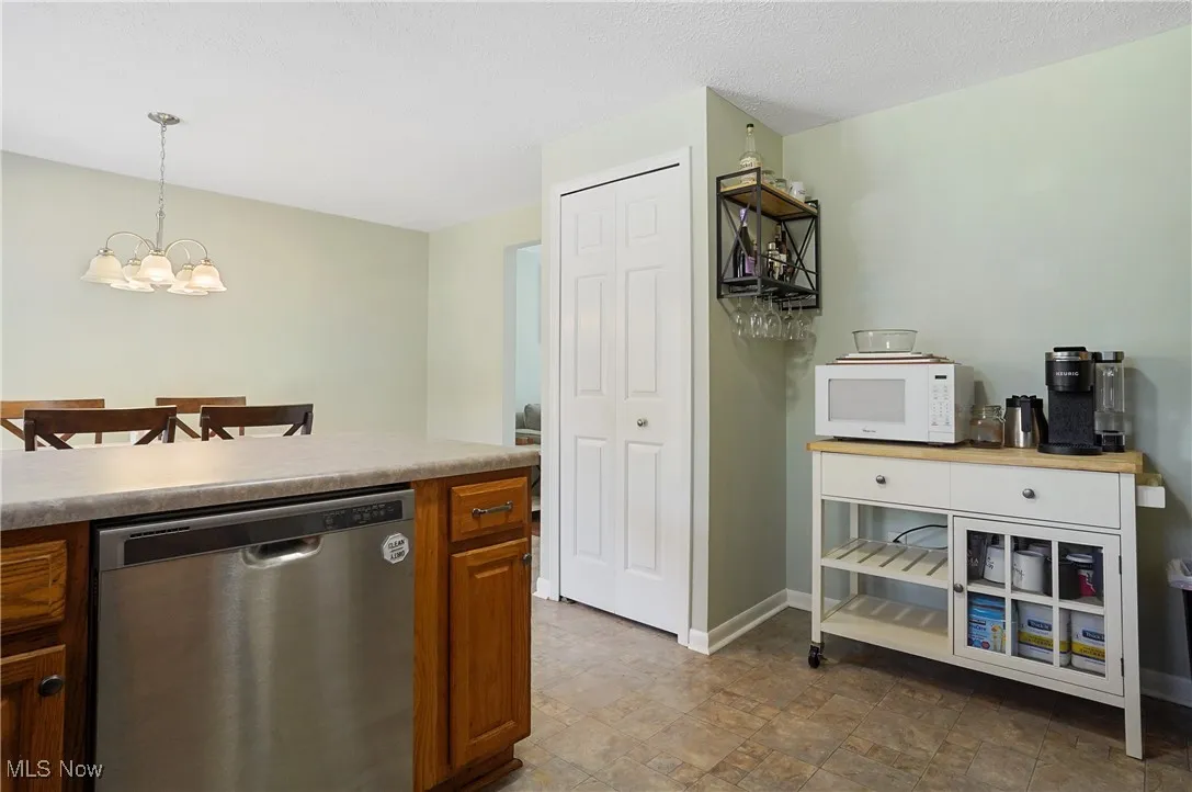 Kitchen featuring stainless steel dishwasher, pendant lighting, white microwave, brown cabinets, and a chandelier