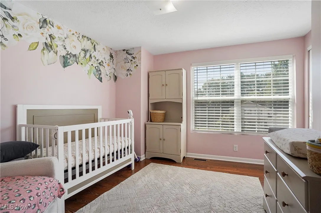 Bedroom with a crib, dark wood-style floors, and a textured ceiling