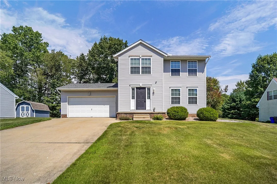 View of front of property featuring an attached garage, concrete driveway, a front yard, and a storage shed