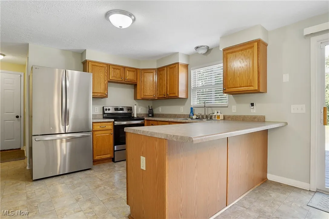 Kitchen featuring appliances with stainless steel finishes, a peninsula, light countertops, and brown cabinets