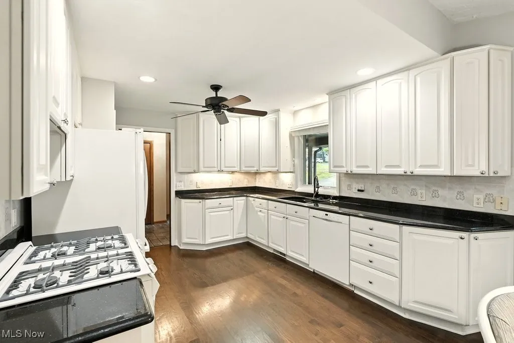 Kitchen with white cabinets, dark wood-style flooring, white appliances, decorative backsplash, and recessed lighting